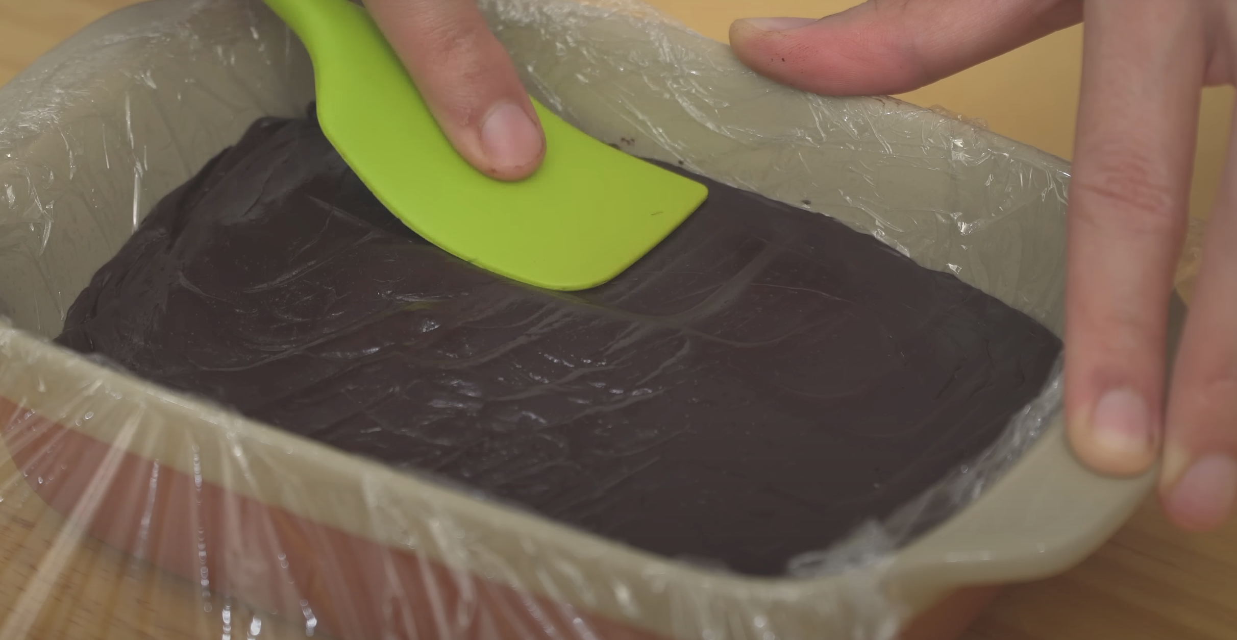 hand using a spatula to press chocolate batter into a container